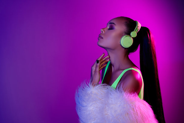 照片中光彩夺目的女士穿着皮草大衣，耳机欣赏歌曲，空旷的空间孤立的紫色背景图片下载