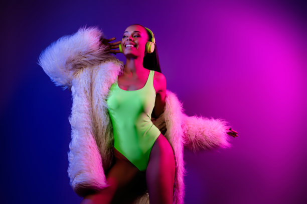 照片中苗条微笑的女士穿着皮草大衣，耳机跳舞，空旷的空间孤立的紫罗兰色背景图片下载