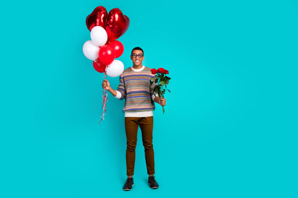 漂亮的年轻人的全尺寸照片拿着鲜花气球穿毛衣孤立的蓝绿色背景图片下载