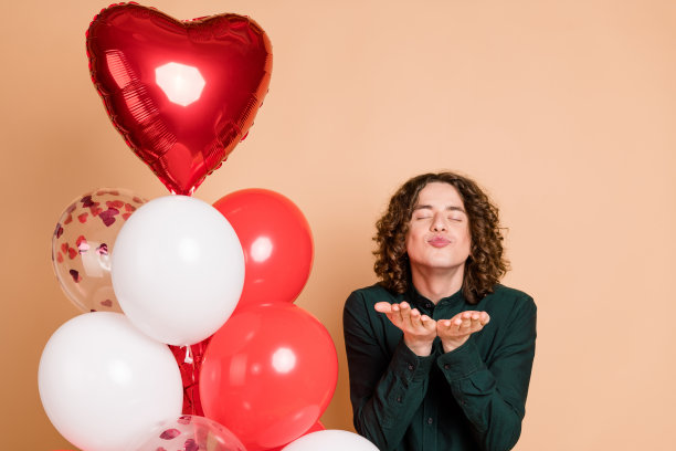 照片中的帅哥情人节气球送飞吻穿着时尚的绿色服装孤立在米色背景图片下载