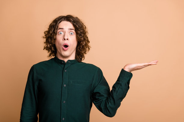 印象深刻的照片惊讶的好男人穿着绿色时髦的衣服hold推荐空白空间孤立在米色背景图片下载
