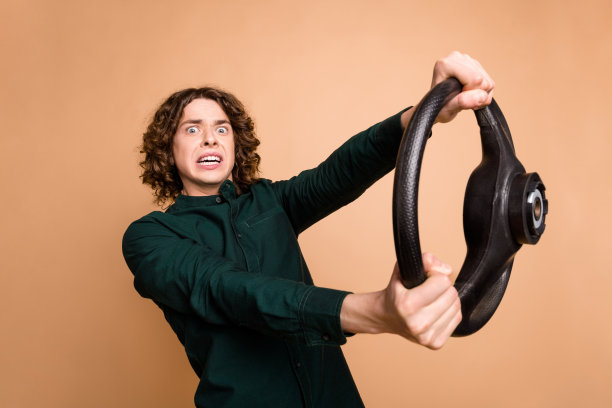 照片肖像英俊的年轻人握着方向盘害怕穿着时髦的绿色服装孤立在米色背景图片下载