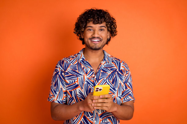 照片肖像英俊的年轻人拿着小玩意，穿着时尚的彩色服装，孤立在橙色的背景图片下载