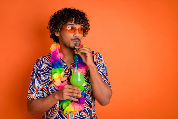 照片中的帅哥享受夏天看空空间喝鸡尾酒穿着时尚的彩色服装孤立在橙色的背景图片下载