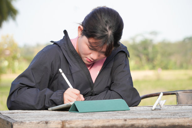 年轻的亚洲女性在户外或公园用平板电脑远程工作。自然光与树木和自然背景。自由职业者的概念。图片下载