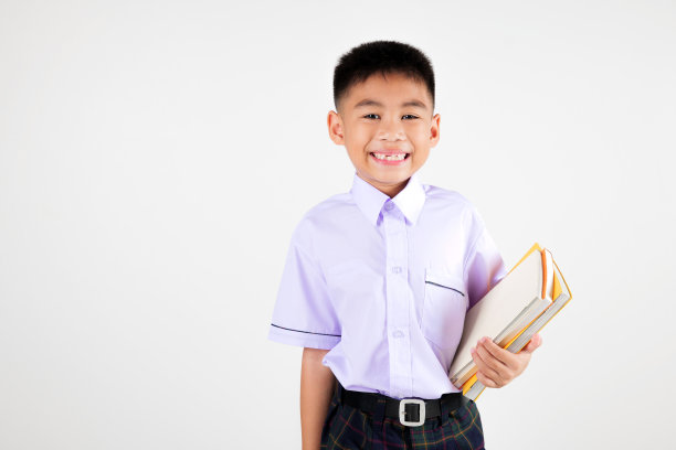 肖像微笑亚洲小男孩初级摆姿势手捧书工作室孤立的白色背景，快乐可爱的男人孩子穿校服格子图片下载