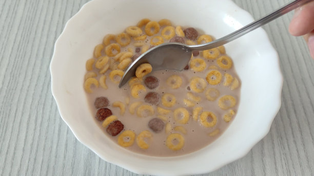 一个不知名的男人用勺子在牛奶里搅拌玉米片、玉米圈和玉米球图片下载