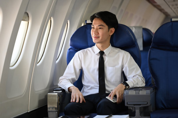 年轻的商人舒适地坐在飞机座位上，带着满足的微笑望着窗外图片下载
