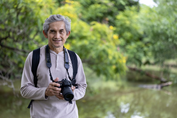 一位亚洲老人在森林里徒步旅行，用相机为老年人户外锻炼和自然环境治疗拍摄难忘的照片图片下载
