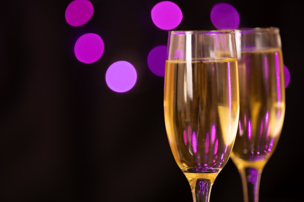 装满气泡的香槟酒杯，排列在图片的右侧。背景以黑色背景和模糊的紫色灯光为背景，唤起了除夕的节日气氛。图片下载
