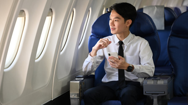 英俊的商人在飞行中拿着手机向窗外看的肖像图片下载