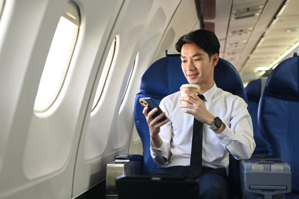 微笑的年轻商人在飞机上使用智能手机。旅游与商务理念图片下载