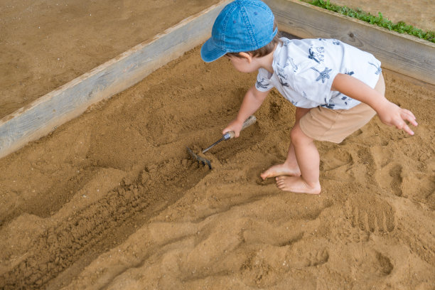 蹒跚学步的孩子在考古公园的沙箱里用耙子挖掘图片下载