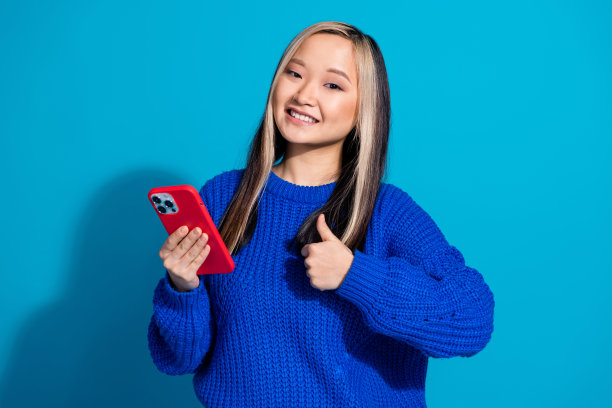 照片肖像的十几岁的女孩在时尚的针织毛衣使用手机博主拇指像孤立的蓝色背景图片下载