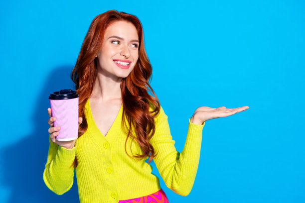 迷人的年轻女孩的照片肖像喝咖啡抱着看空空间穿着时尚的黄色衣服孤立在蓝色的背景图片下载