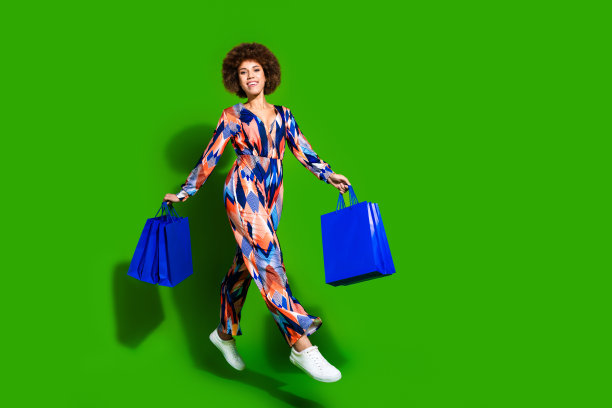 照片中漂亮可爱的女人穿着时髦的衣服，拎着购物，走着商店，在绿色的背景上孤立起来图片下载