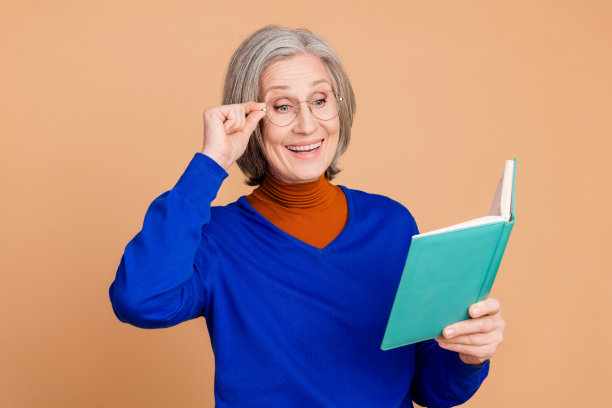 漂亮的高级妇女的照片肖像阅读兴奋的书穿着时髦的蓝色服装孤立的米色背景图片下载