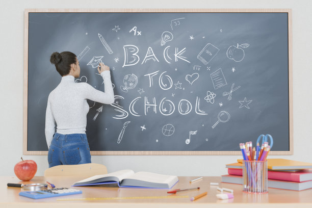 老师在黑板上写着“回到学校”，课桌上放着学习用品图片下载