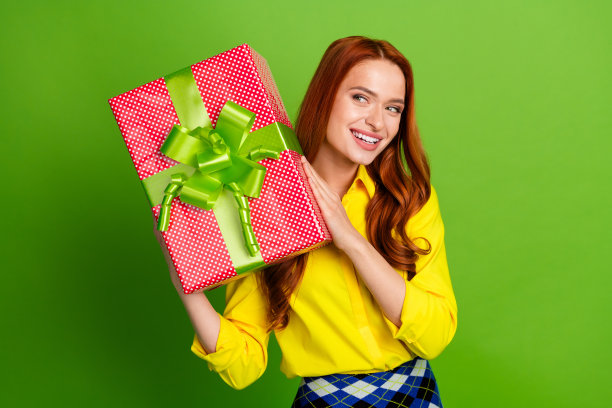 照片中漂亮可爱的女人穿着黄色时髦的衣服，拿着包裹，在绿色的背景上看起来空无一物图片下载