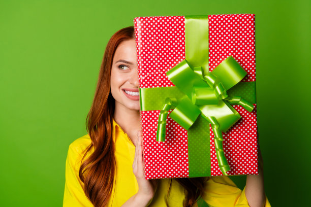 照片中开朗的漂亮可爱的女人穿着黄色时髦的衣服接受礼物，在绿色的背景上看起来空无一物图片下载