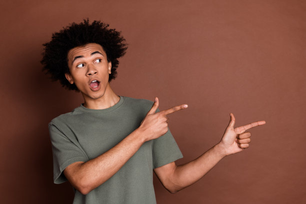年轻男子的肖像照片，穿着灰色t恤，头发卷曲，正手指空白，惊讶地孤立在棕色背景上图片下载
