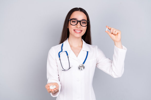照片迷人迷人的女人合格的专科治疗师穿着白色的医生长袍，手持药丸隔离在灰色背景图片下载