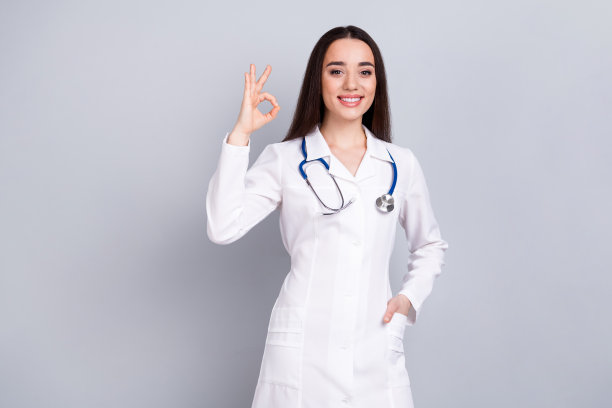 专业医务工作者女士的照片显示大拇指朝上，白色外套孤立在灰色背景上图片下载