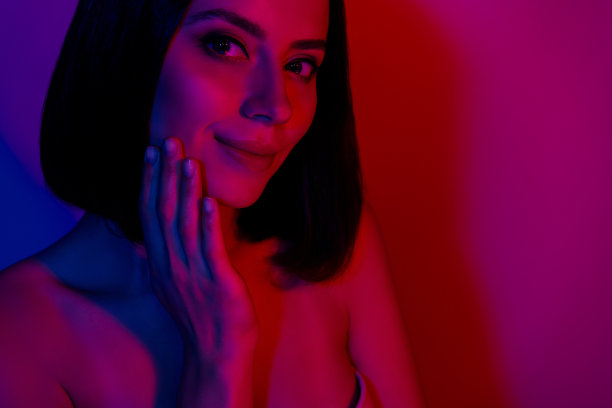 照片中快乐的女孩抚摸手指的脸享受嫩肤孤立的霓虹彩色背景图片下载