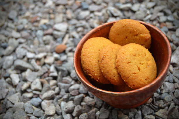 灰色的彩色鹅卵石水平照片与各种大小不均匀的石头，使一个粗糙的乡村背景壁纸与各种颜色的小石头和一个圆形的木碗充满了美味可口诱人的饼干或饼干图片下载