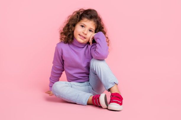 时髦迷人的小孩穿着紫色套头衫坐在地板上微笑孤立的粉红色背景的全长照片图片下载