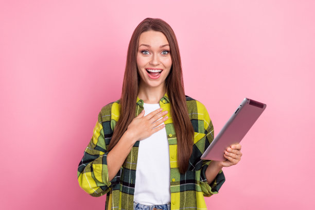 有趣的女孩时髦的照片穿着时髦的黄色格子夹克触摸胸部心脏拿平板电脑意想不到她的统计孤立在粉红色的背景图片下载