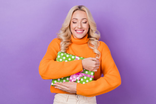 照片开朗可爱的女士闭上眼睛，牙齿微笑，手臂抱抱礼盒孤立的紫罗兰色背景图片下载