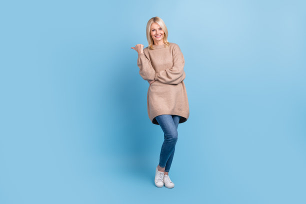 乐观迷人的女商人穿米色毛衣的全身照片直接手指广告横幅孤立的蓝色背景图片下载