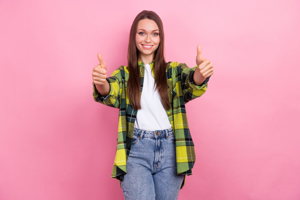 照片的华丽开朗的女人与长发型，穿格子衬衫，显示拇指向上，很好的工作孤立在粉红色的背景图片下载