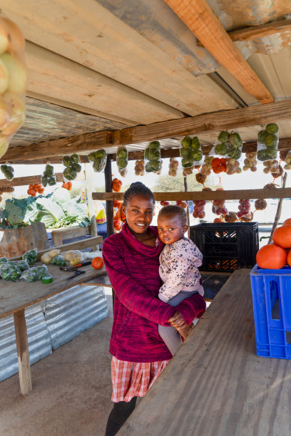 非洲农村的妇女抱着她的孩子，沿街叫卖水果，一袋袋的橙子、卷心菜、青椒、洋葱、西红柿、菠菜，在乡路上卖图片下载