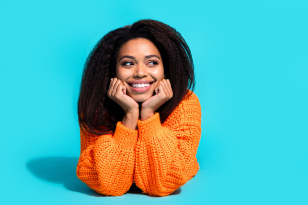 照片中，迷人的年轻女子躺在地板上，看起来空荡荡的，穿着时尚的针织橙色衣服，孤立在蓝色的背景上图片下载