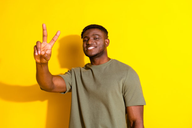 照片中开朗开朗的帅哥穿着卡其色时髦的衣服，v字标志孤立在黄色背景上图片下载