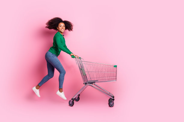 可爱的年轻女士推着超市推车的照片肖像，在粉红色的背景上穿着时尚的绿色服装图片下载