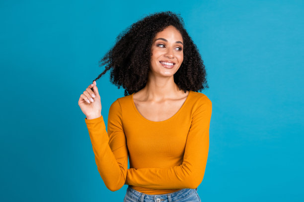 可爱的年轻女士的照片看起来空旷的空间，拿着头发，发型穿着时尚的橙色服装，孤立在蓝色的背景图片下载