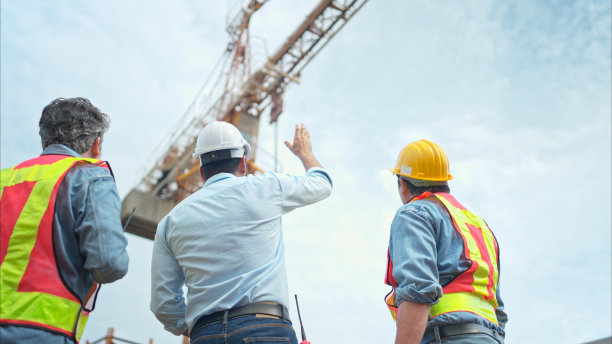 图为，工地上的工人们正在讨论施工进度，背景是塔吊图片下载