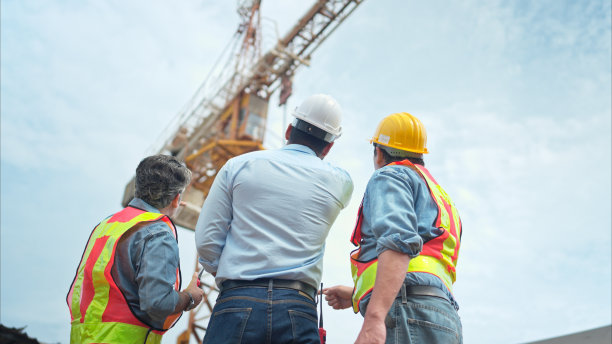 图为，工地上的工人们正在讨论施工进度，背景是塔吊图片下载