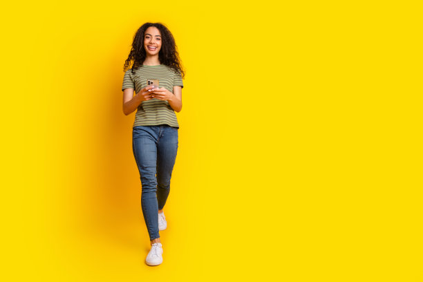 乐观的好心情女孩的全尺寸照片，穿着t恤，拿着智能手机，在黄色背景上阅读电子邮件图片下载