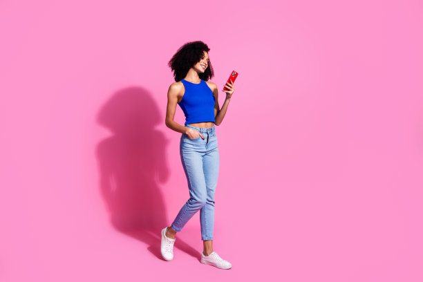 照片中的女孩微笑着走路，使用手机智能设备，看起来孤立的粉彩背景图片下载