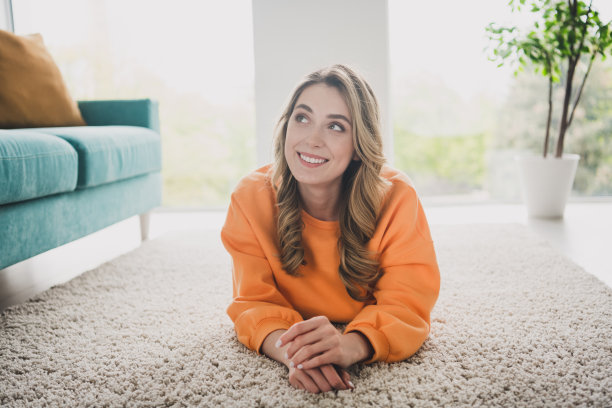 漂亮的年轻女子的全尺寸照片躺在地板上看起来梦幻的空间穿着橙色的衣服舒适的日光家室内客厅图片下载