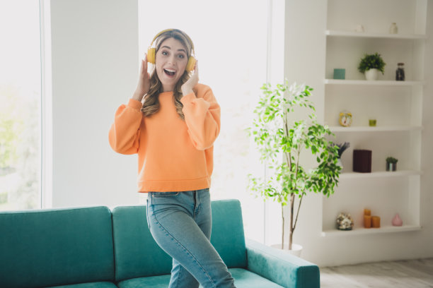 照片肖像迷人的年轻女子耳机听音乐兴奋穿着橙色的衣服舒适的日光家室内客厅图片下载