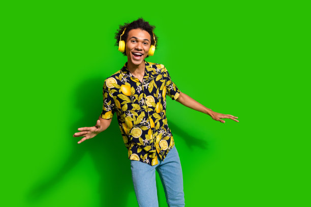 开朗积极的男人的照片，穿着时尚的印花服装，享受听音乐，有乐趣孤立的绿色背景图片下载