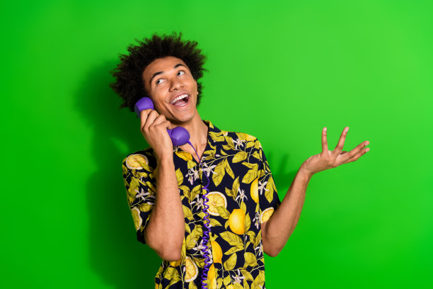 照片中开朗的快乐有趣的男人穿着时髦的印花衣服，拿着说话的电话，在绿色的背景上仰望空旷的空间图片下载