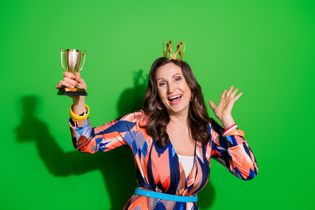 照片中可爱的女子穿着五彩缤纷的整体迪马，手持冠军奖杯，空旷的空间孤立的绿色背景图片下载