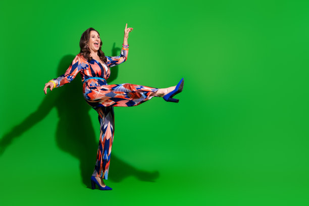 全身照片可爱可爱的女人穿五彩缤纷的整体舞蹈迪斯科舞厅空的空间孤立的绿色背景图片下载
