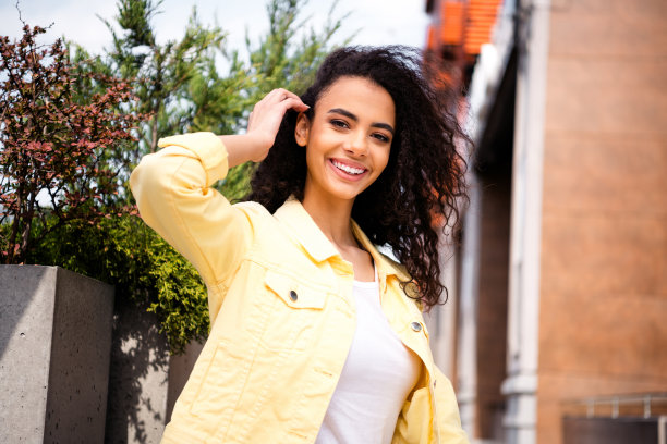 照片中的年轻积极的少女触摸波浪发型的学生呼吸新鲜空气，穿黄色时尚夹克花时间在户外周末图片下载
